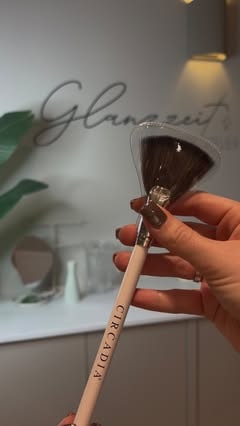 Hand mit Kosmetikpinsel vor dem Glanzzeit-Schriftzug